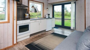 A compact kitchen with a stove, oven, and sink, wooden walls, and a large sliding glass door to a garden.