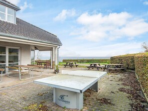 An outdoor seating area with tables and chairs, a covered pavilion, and a view of the sea.