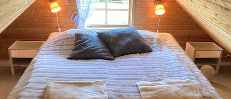 A cozy attic bedroom with a bed, two bedside tables, and a window with curtains.