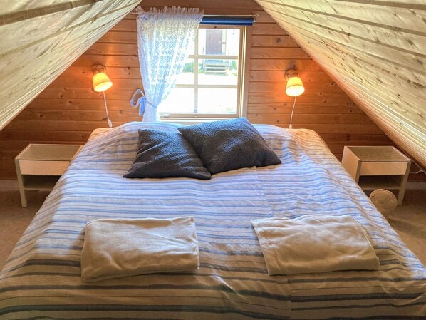 A cozy attic bedroom with a bed, two bedside tables, and a window with curtains.