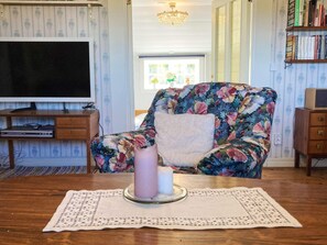 A cozy living room with a floral armchair, a flat-screen TV, a bookshelf, and a table with a candle. - 6 Person Holiday Home in Hagby (Ljungbyholm)