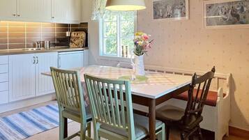 A kitchen with white cabinets, a tiled backsplash, a window with a lace curtain, and a dining table with chairs.