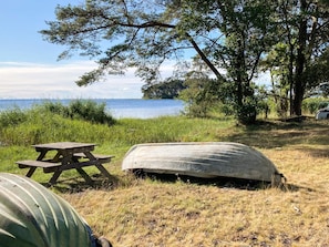 A picnic table and a large stone slab in a grassy area with trees and a body of water in the background.