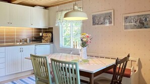 Ett kök med vita skåp, ett matbord med en rutig duk och två stolar.