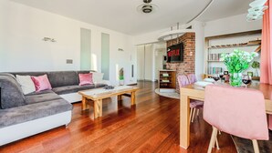 Una sala de estar moderna con un sofá gris, una mesa de centro de madera y una zona de comedor con una silla rosa.
