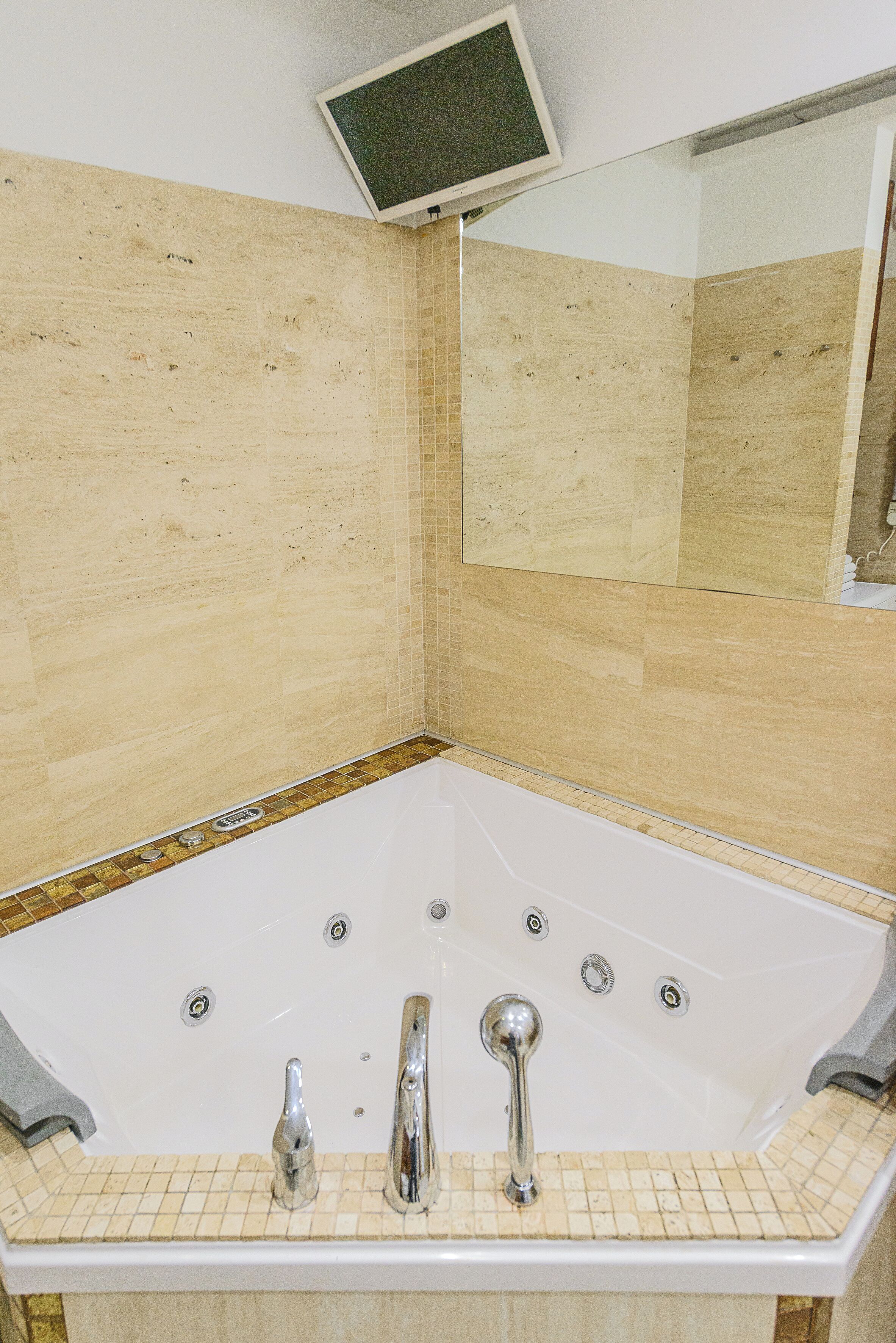 Ein Badezimmer im Eckbereich mit freistehender Badewanne, einem Spiegel darüber und gefliesten Wänden.