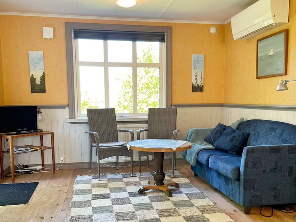 A room with a blue sofa, two chairs, a small table, a TV on a stand, and a window with blinds. - 6 Person Holiday Home in Borgholm (Borgholm)
