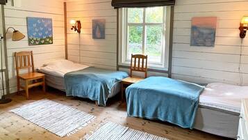 A room with two beds, wooden flooring, and a window with a view.
