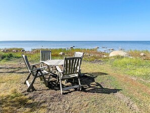 A wooden table and chairs set on a grassy area with a view of the sea and rocks. - 6 Person Holiday Home in Borgholm (Borgholm)