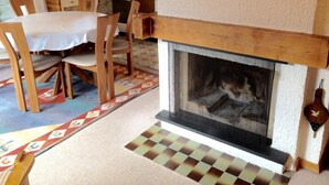 A cozy living room with a fireplace, wooden furniture, and a patterned rug. - Apartment in Veysonnaz Near Ski Gondola (Veysonnaz)