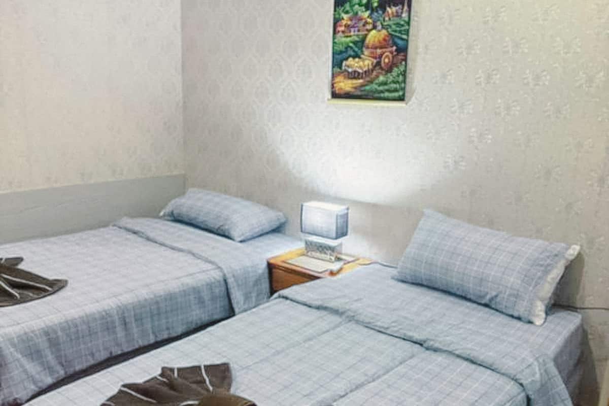 A room with two beds, a small bedside table with a lamp, and a wall-mounted air conditioner.
