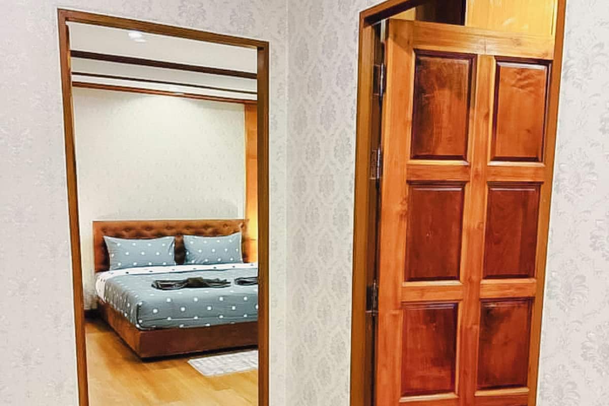 A bedroom with a wooden door, a bed with a blue polka dot bedspread, and a wooden floor.