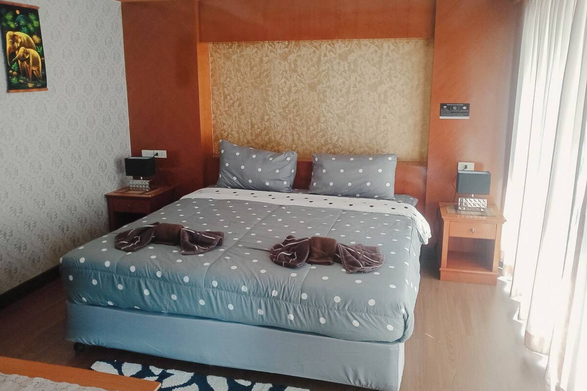 A bedroom with a large bed, two pillows, a nightstand, a lamp, and a painting on the wall.
