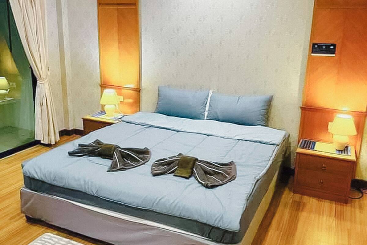 A neatly made bed with pillows, a bedside table with a lamp, and a wooden floor.