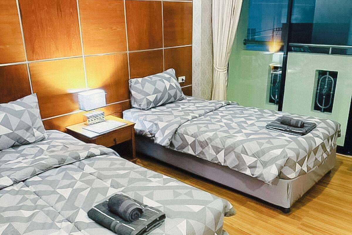 A hotel room with two beds, wooden paneling on the walls, a nightstand, and a view of the city through a large window.