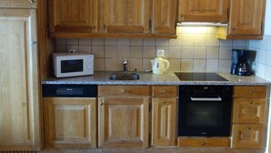 A kitchen with wooden cabinets, a microwave, a kettle, a coffee maker, and a dishwasher. - Apartment in a Central Location (Veysonnaz)