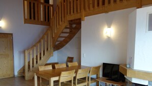 A wooden staircase, a dining table with chairs, a television, and a fireplace. - Apartment in a Central Location (Veysonnaz)