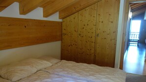 A bedroom with a wooden headboard, a bed with white bedding, and a wooden wardrobe. - Apartment in a Central Location (Veysonnaz)