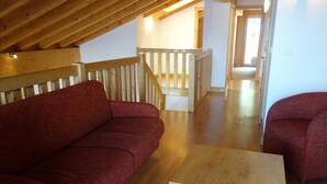 A room with a wooden ceiling, a red sofa, a wooden coffee table, and a staircase leading to another level. - Apartment in a Central Location (Veysonnaz)