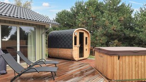 Um deck de madeira com duas banheiras de hidromassagem, uma sauna e um espaço envidraçado.