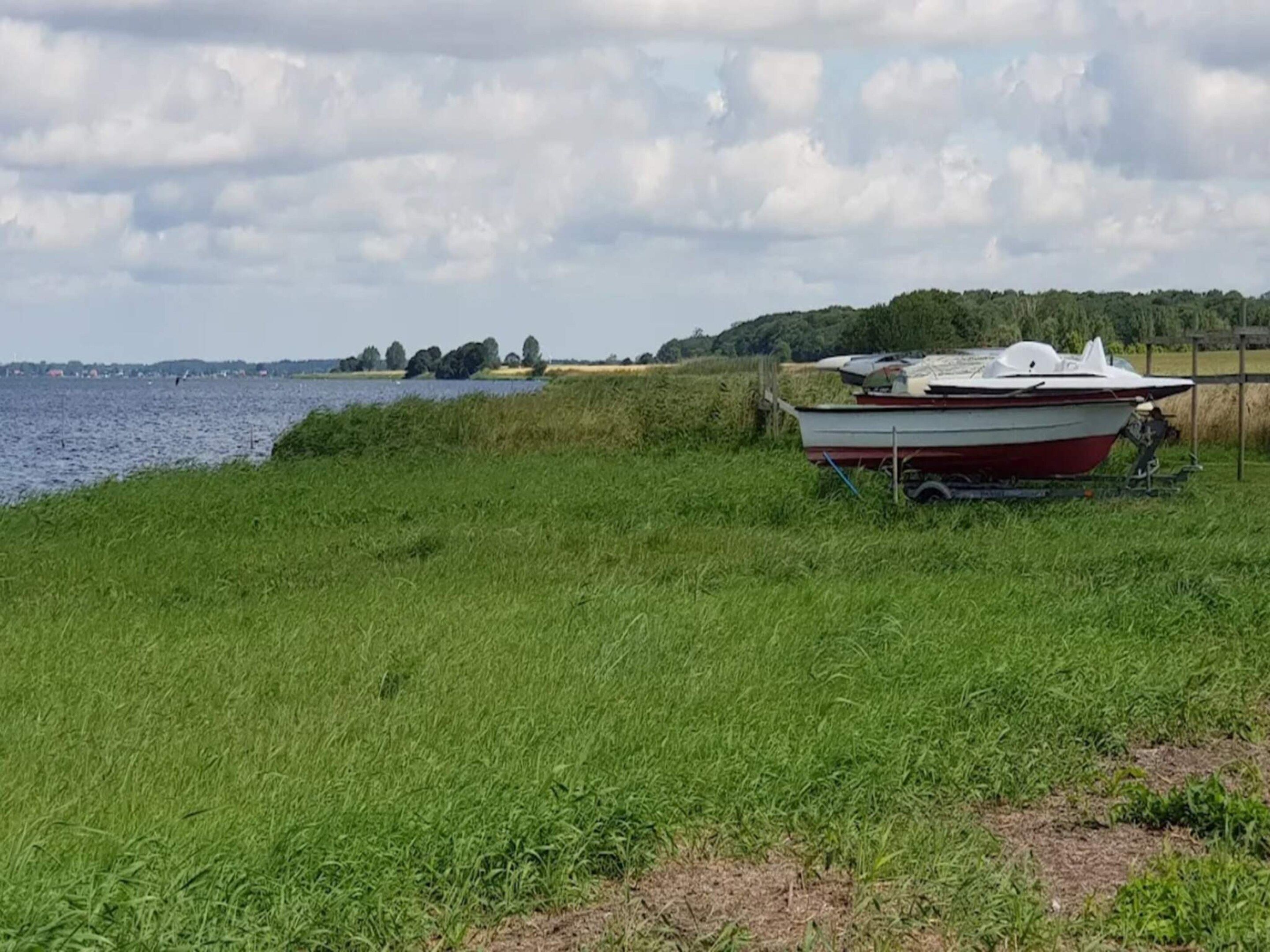 A grassy area with a boat on a trailer near a body of water.