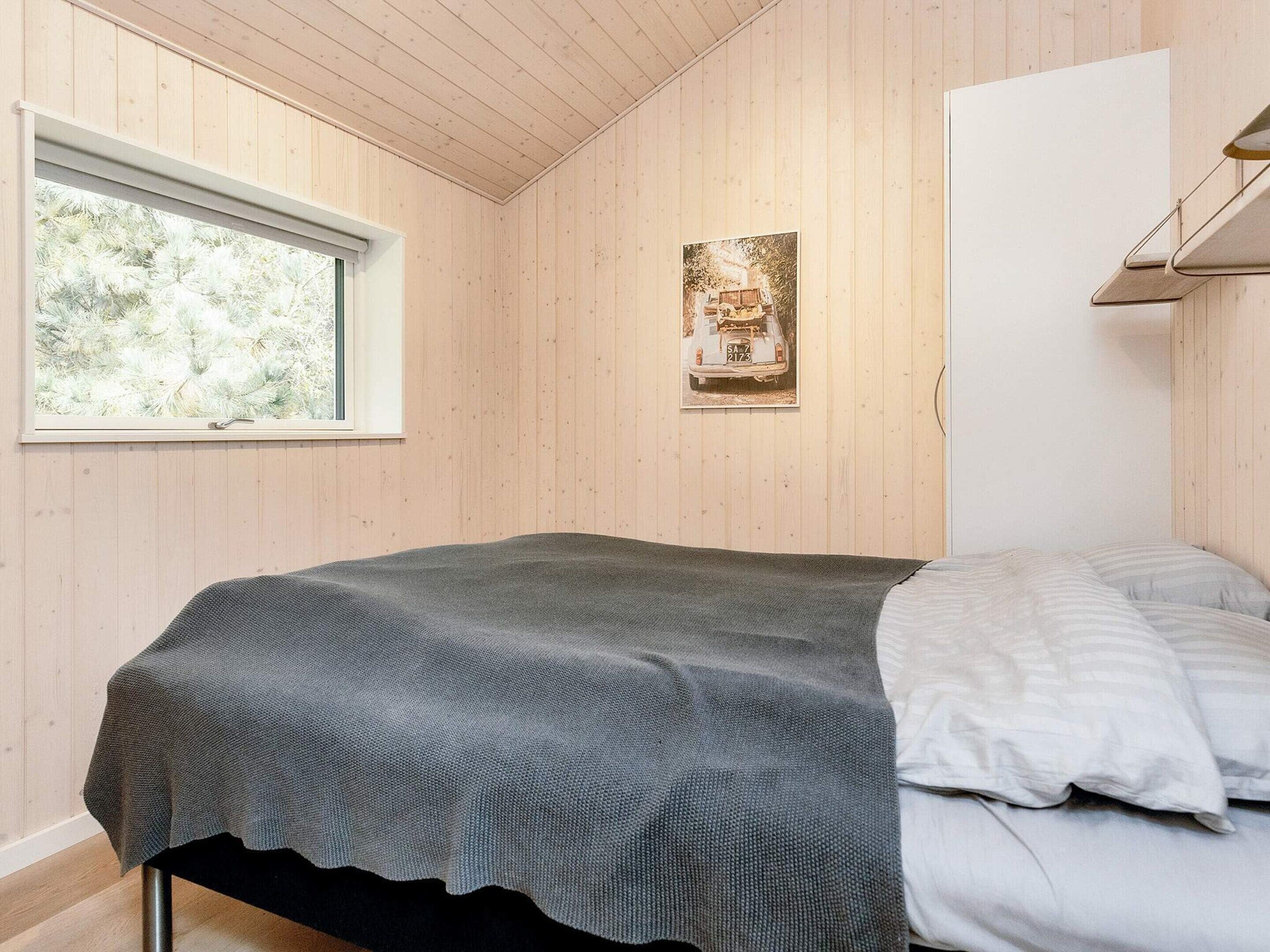 A bedroom with a bed, a window, and a wall-mounted picture.