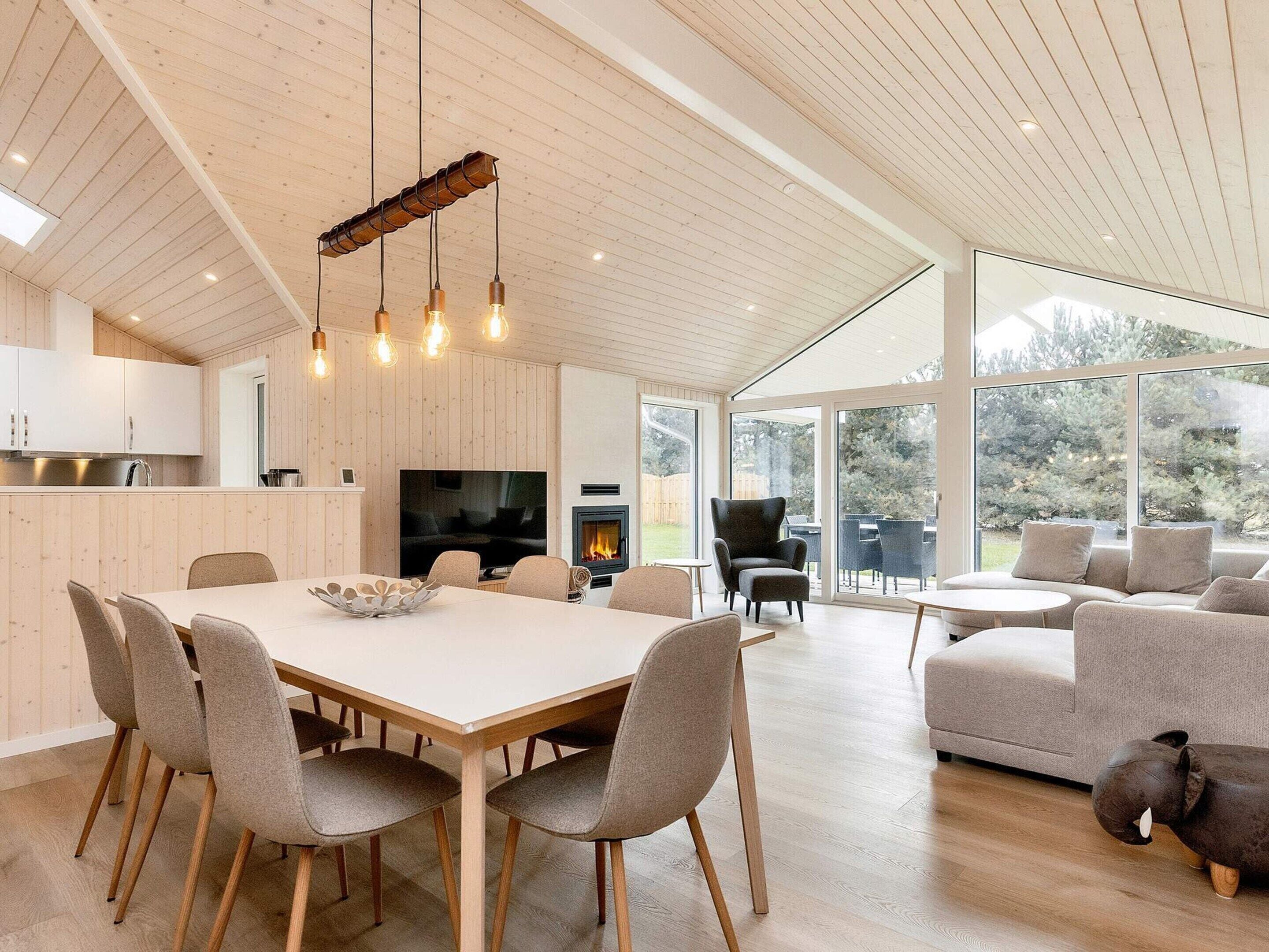 A modern interior with a dining area, a fireplace, and a large window overlooking a garden.