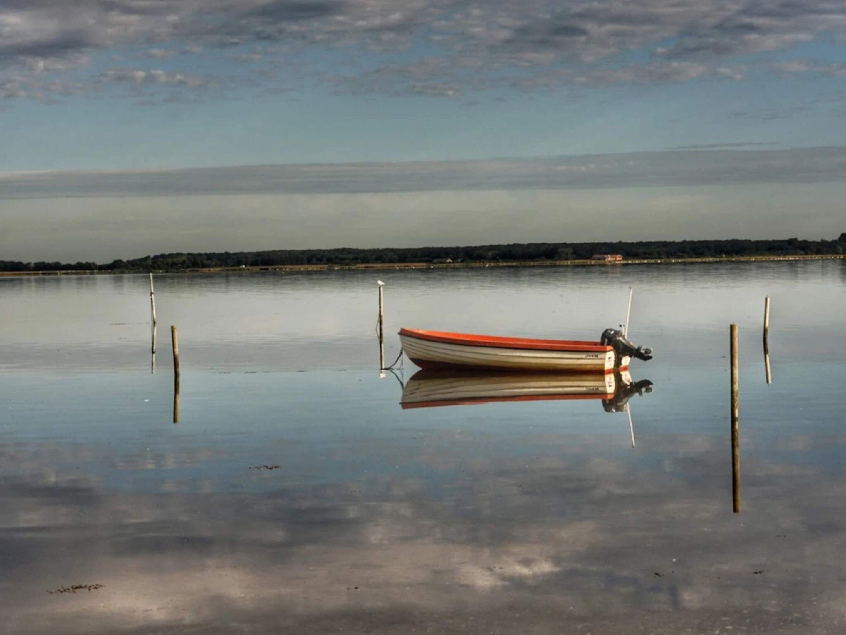 Une étendue d’eau calme, avec une petite barque ancrée près du rivage, entourée d’eau paisible et d’une côte lointaine.