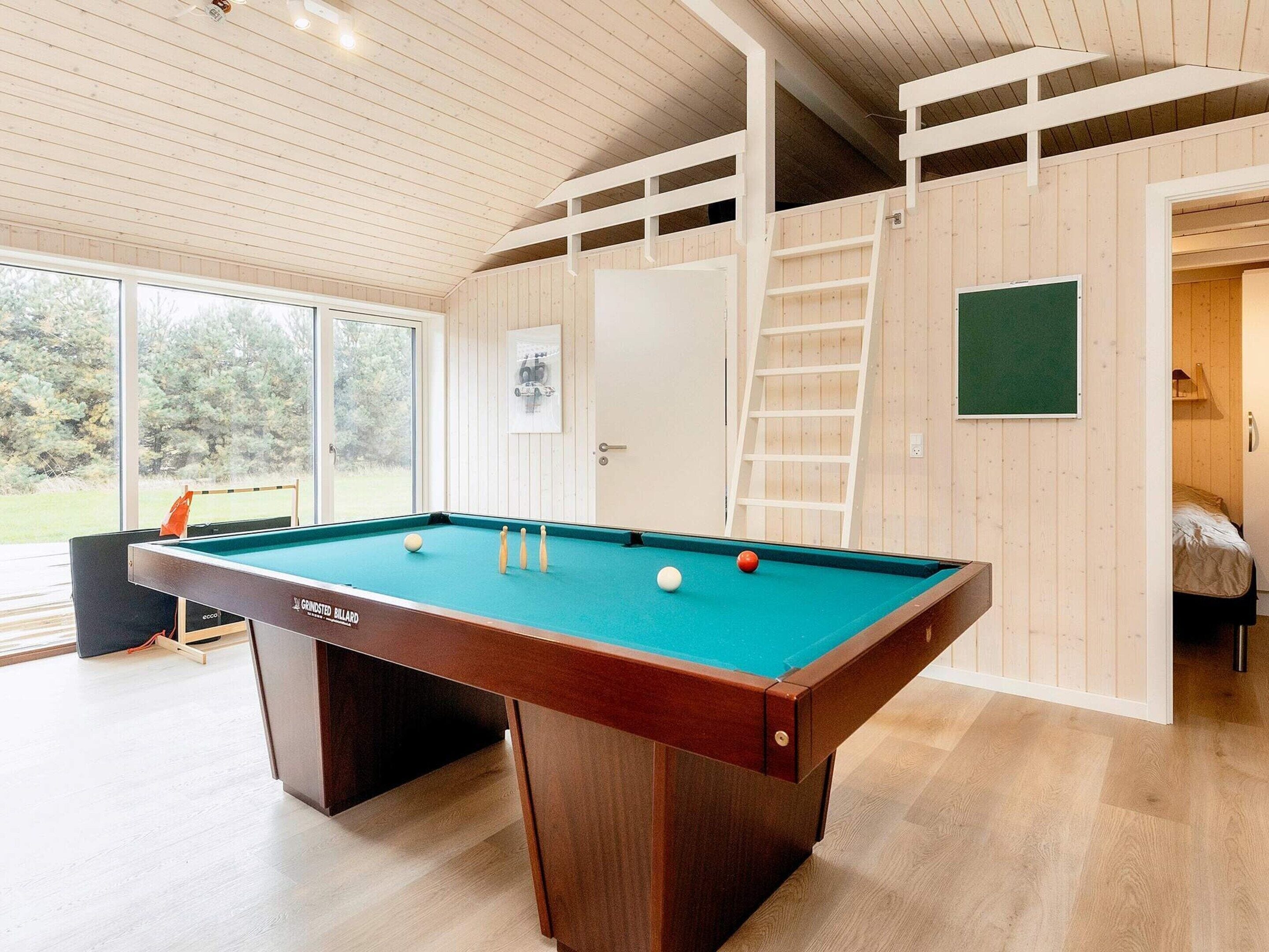 A pool table with balls, a ladder, and a door leading to a bedroom.