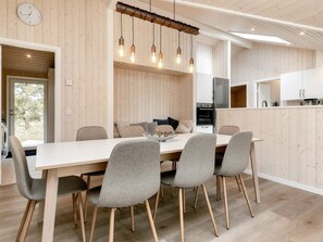 A modern kitchen with wooden paneling, a dining area with a white table and grey chairs, and a hanging light fixture. - 5 Star Holiday Home in Vaeggerlose (Vaeggerlose)