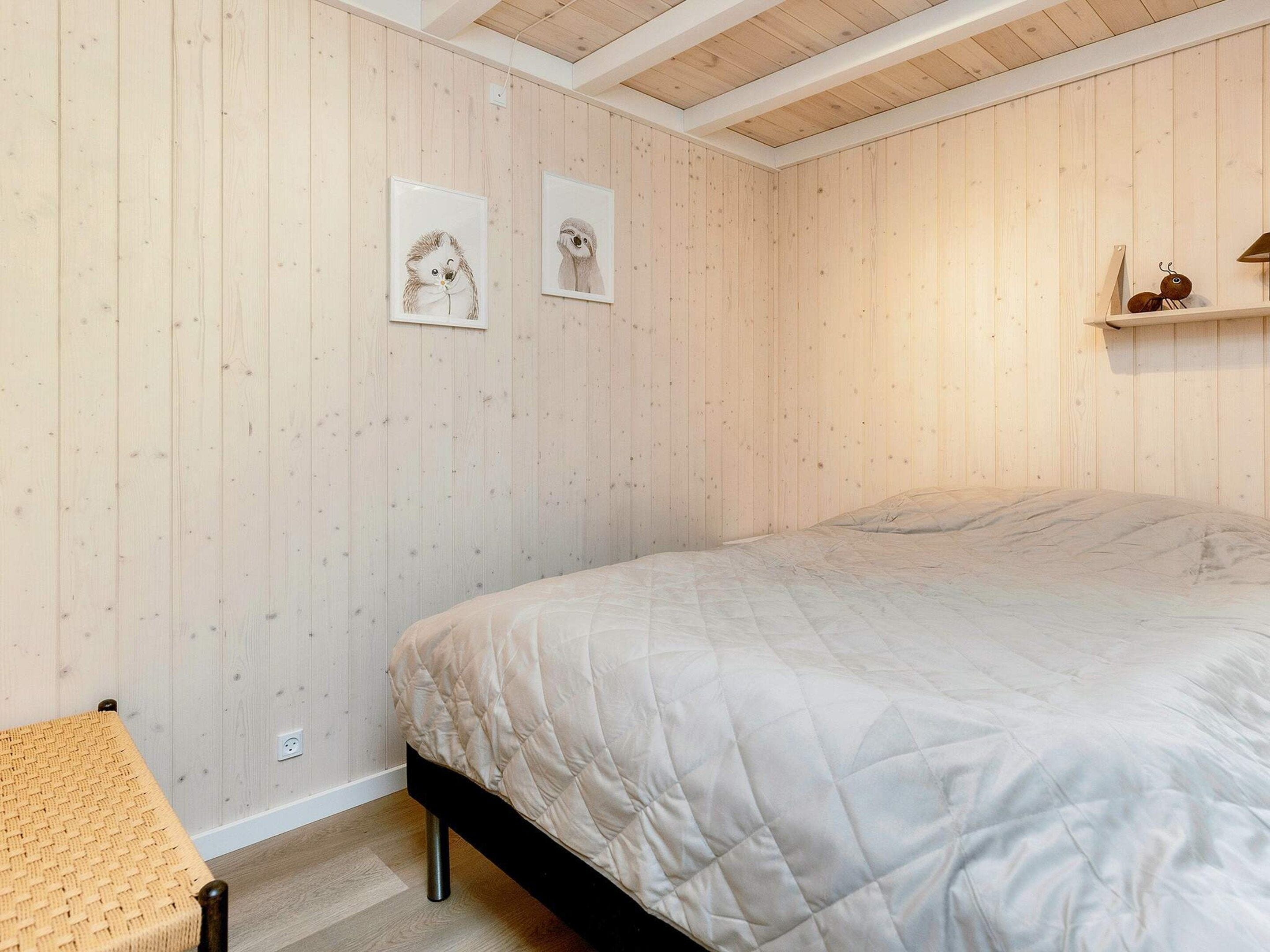 A bedroom with a bed, a bedside table, and two framed pictures on the wall.