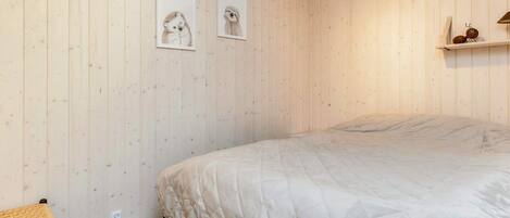 A bedroom with a bed, a bedside table, and two framed pictures on the wall.