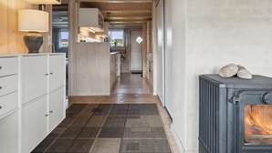 A narrow hallway with a wooden floor, a white cabinet with drawers, a stove with logs, and a view into a room with a bed and window. - "Bjarni" - 175m from the sea by Interhome (Malling)