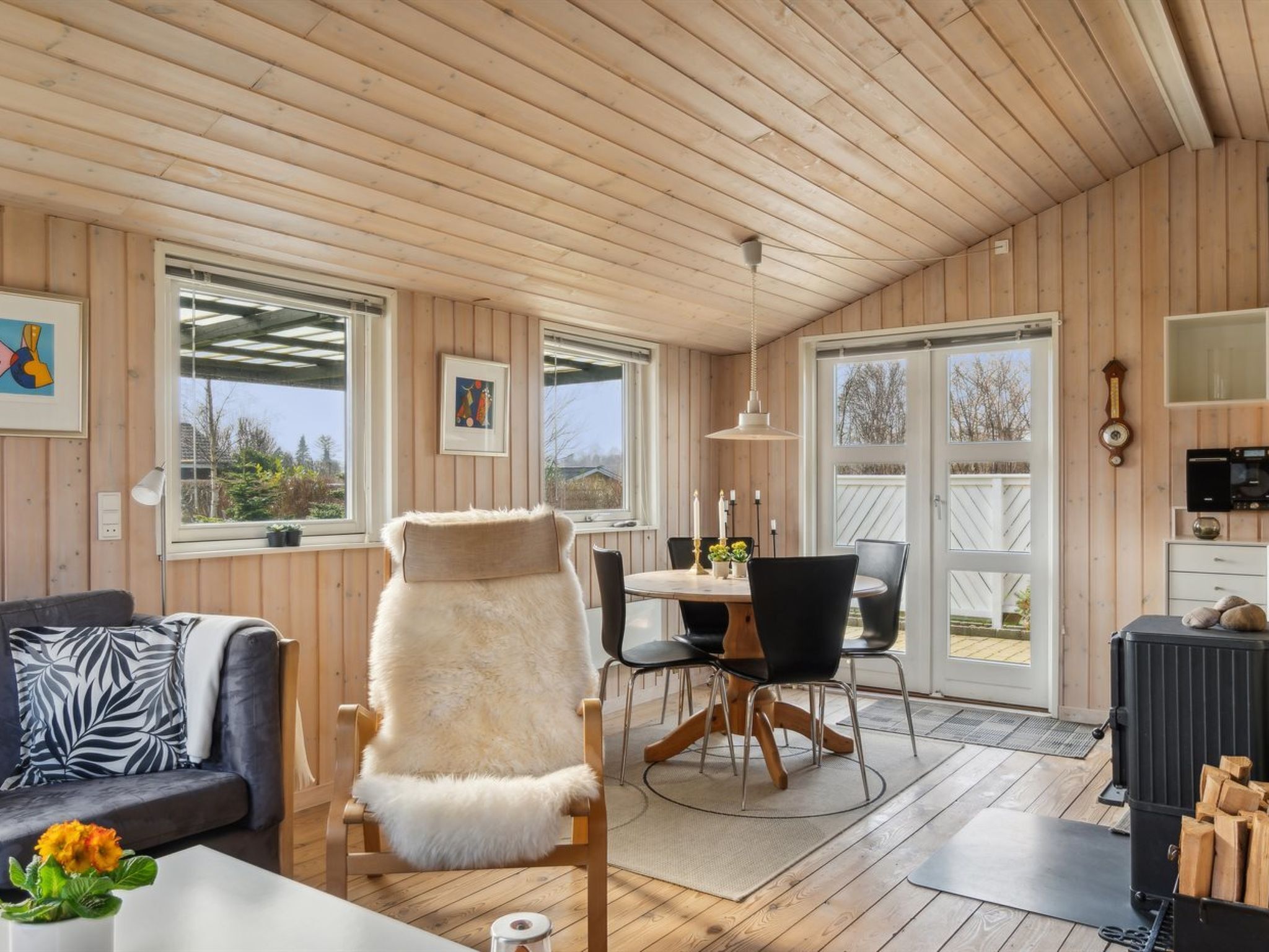 A cozy cabin interior with a wooden ceiling, a fur-covered chair, a dining table with chairs, and a fireplace.