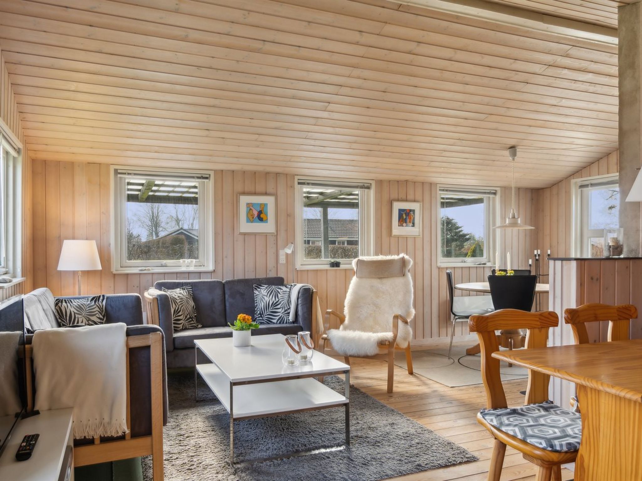 A cozy living room with a sofa, armchairs, a coffee table, and a dining table. There are windows with artwork on the walls.