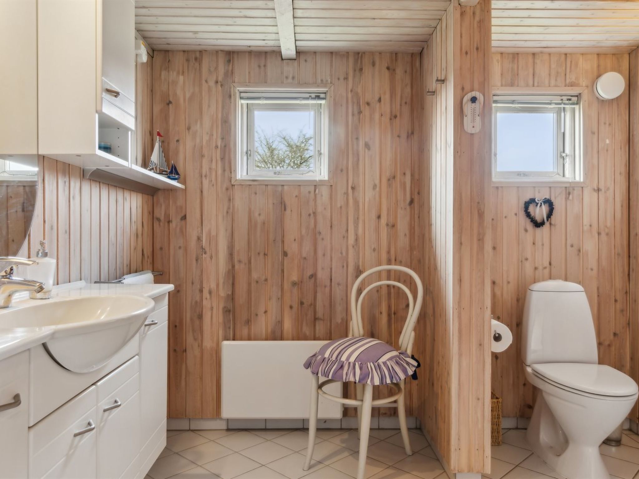 A bathroom with wooden walls, a white sink, a toilet, and a chair.