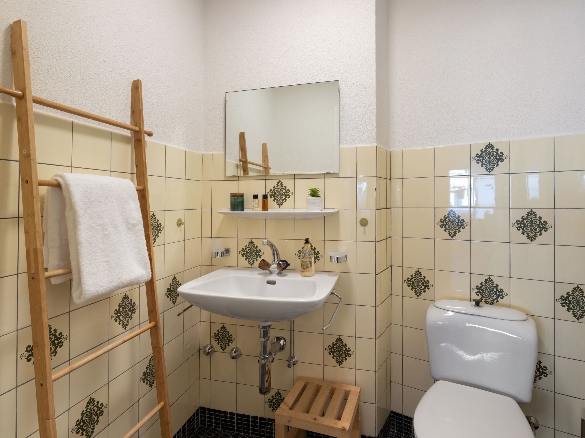 Een badkamer met een houten handdoekhouder, een wastafel, een spiegel, een toilet en decoratieve tegels.