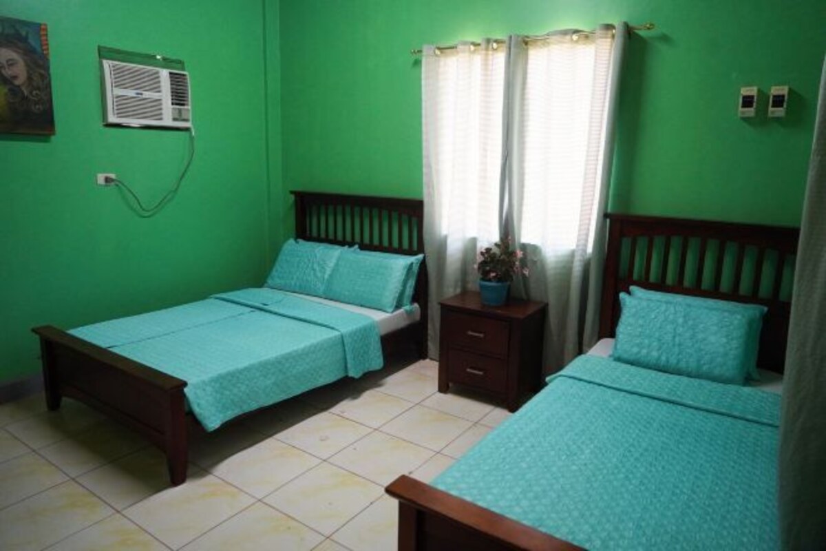 A bedroom with two single beds, a nightstand, a wall-mounted air conditioner, and a window with curtains.