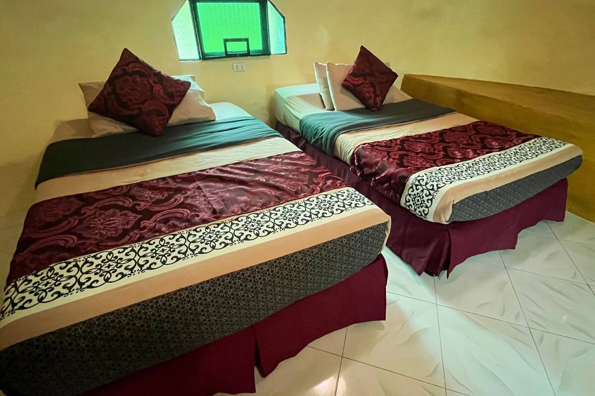 Dos camas individuales con cubrecamas estampadas, una ventana con vistas y un suelo de baldosas.