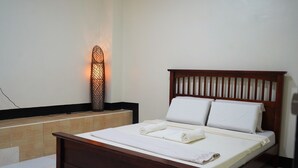 Un lit bien fait, avec du linge de lit et des serviettes blanches, une tête de lit en bois et un luminaire fixé au mur.