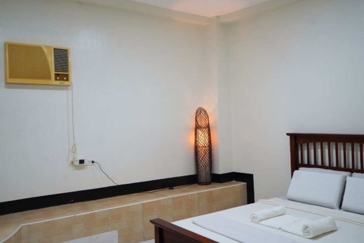 A hotel room with a bed, a wall-mounted heater, and a power outlet.