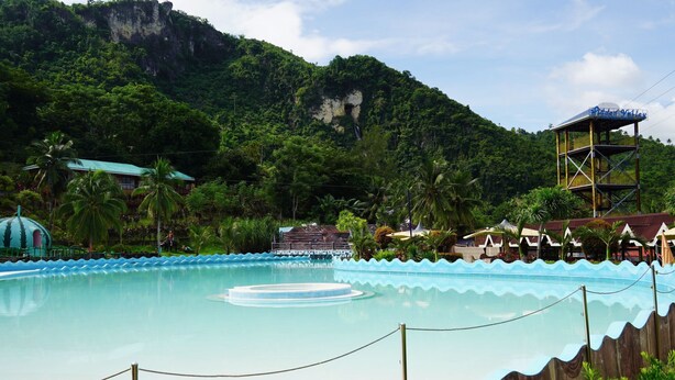 Une piscine dotée d’une terrasse en bois, entourée d’une végétation luxuriante et avec une chaîne de montagnes en toile de fond.