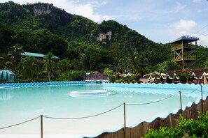 Une piscine dotée d’une terrasse en bois, entourée d’une végétation luxuriante et avec une chaîne de montagnes en toile de fond.