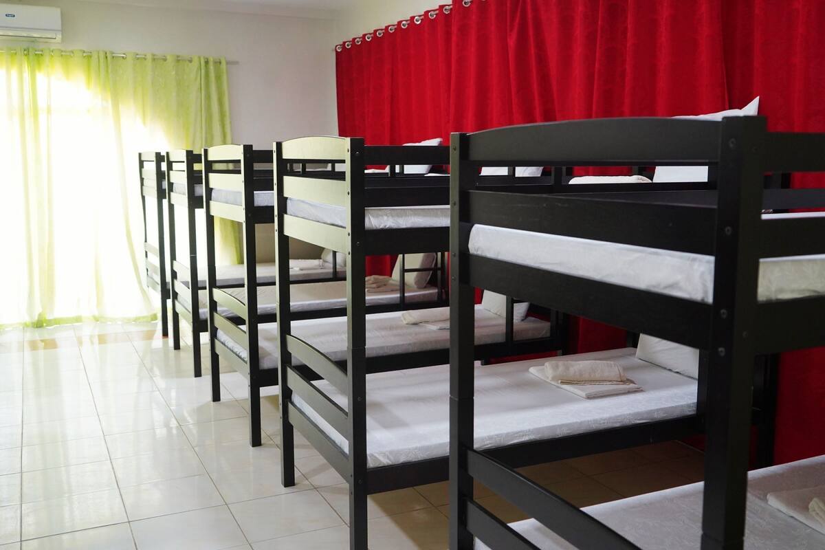 Camas literas en una habitación con una cortina roja y un ventanal con cortinas verdes.