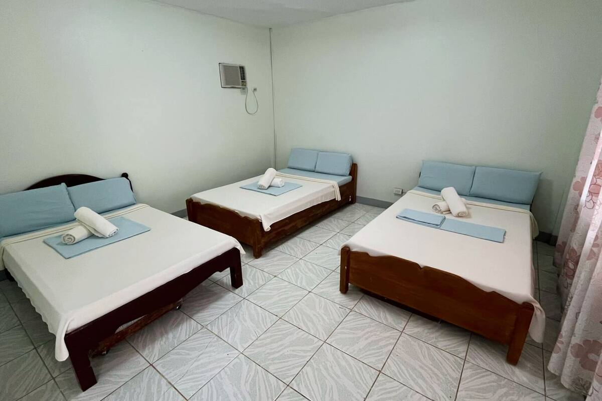 Una habitación con tres camas individuales, cada una con una almohada azul y una manta blanca.