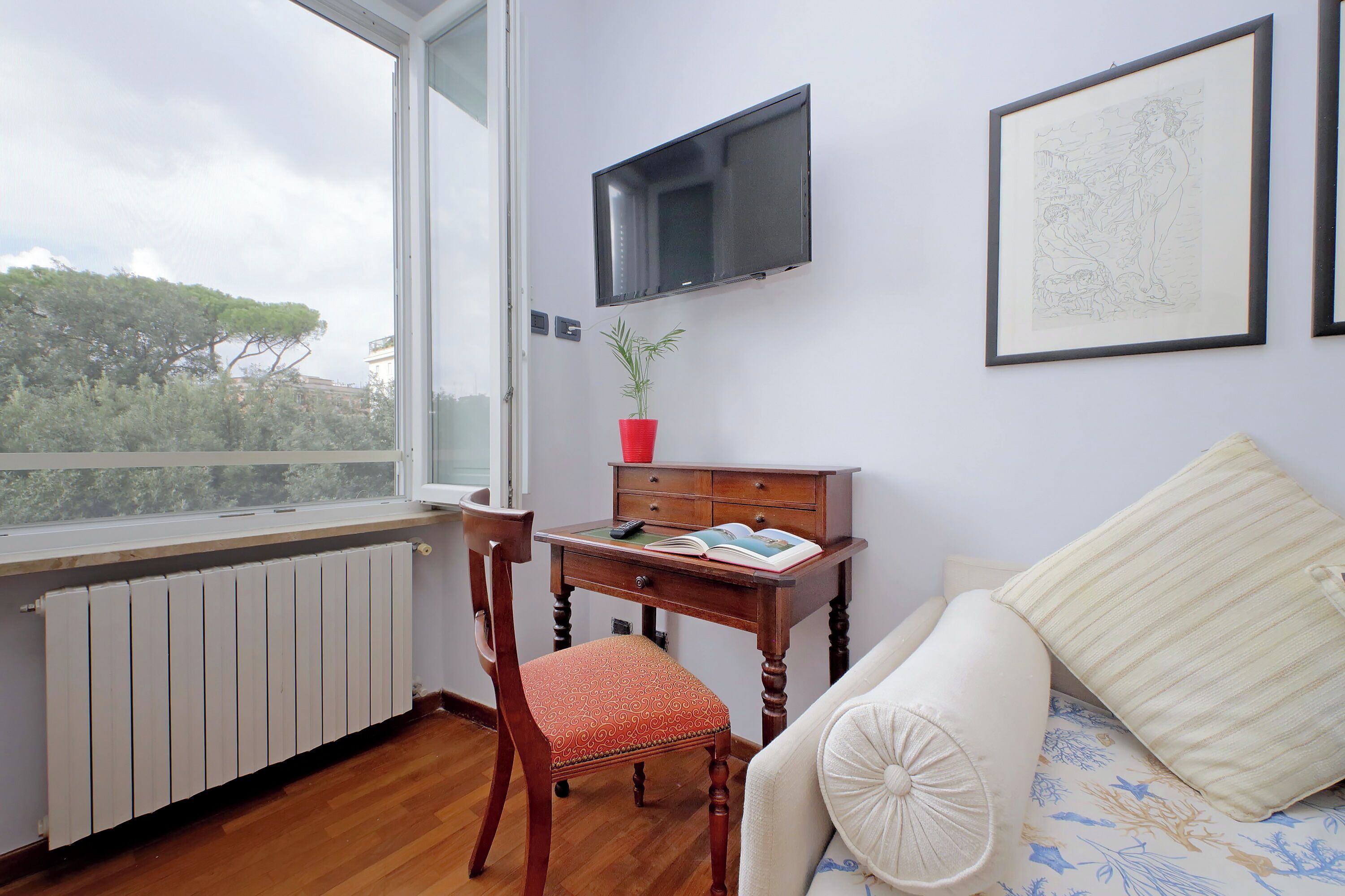 Une chambre avec un bureau en bois, une chaise, un lit avec un oreiller blanc, un téléviseur fixé au mur et une œuvre d’art encadrée.