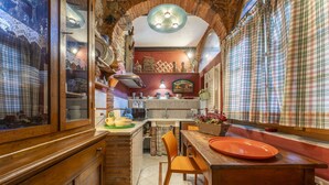 Una cocina con armarios de madera, pared de ladrillo y un comedor con mesa de madera y sillas naranjas.