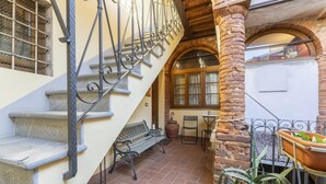 Una escalera de piedra con barandillas de metal, un banco, una mesa y sillas en un patio con baldosas.