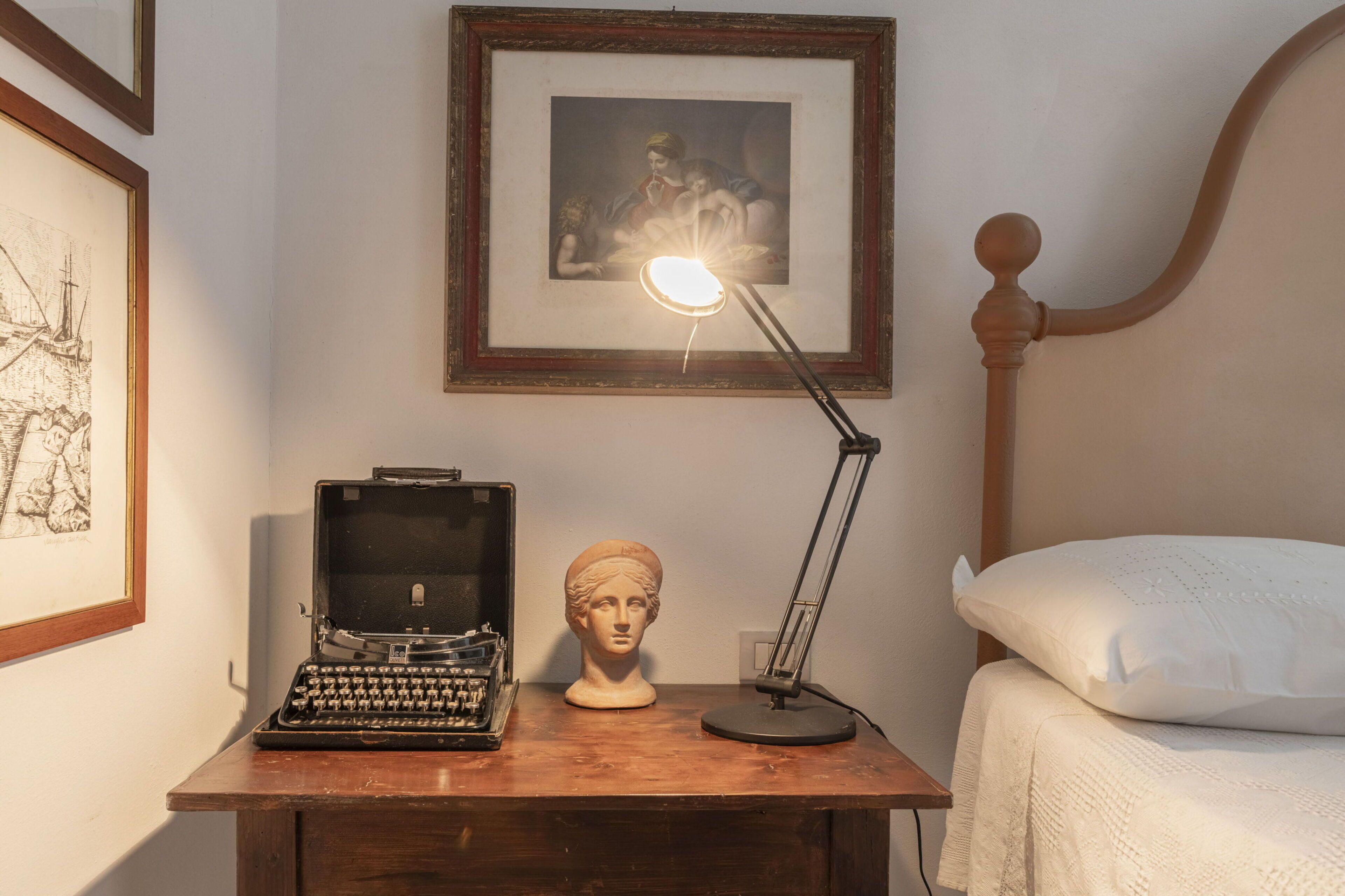 A wooden desk with a typewriter, a bust, and a desk lamp.