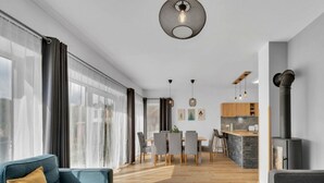 Een moderne woonkamer met een bank, eethoek, keuken en een groot raam met gordijnen.
